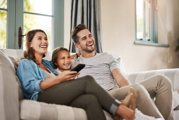 Eine Familie sitzt auf dem Sofa und schaut TV. 