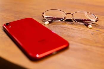 Rotes iPhone liegt auf einem Tisch neben einer Lesebrille