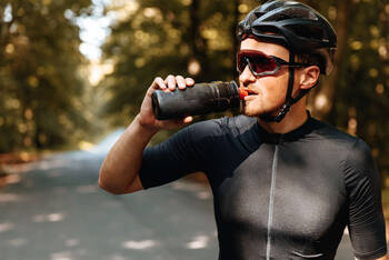 Radfahrer mit Sonnenbrille trinkt aus Trinkflasche