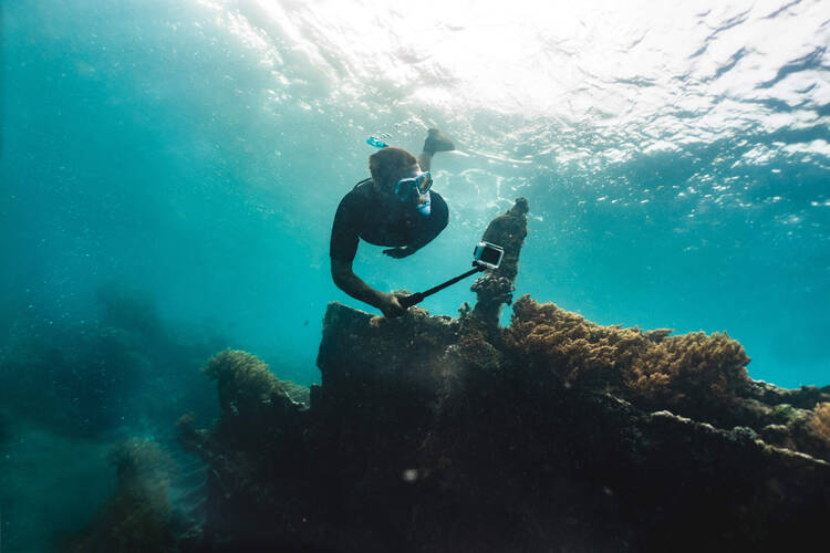 Ein Taucher schwimmt im Meer und filmt sich dabei mit einer Actionkamera.