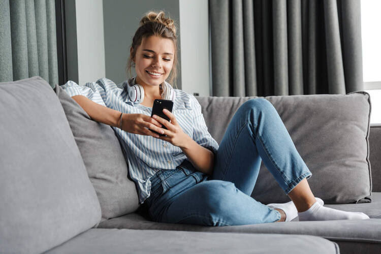 Eine Frau sitzt auf dem Sofa und schaut auf ihr Smartphone. 