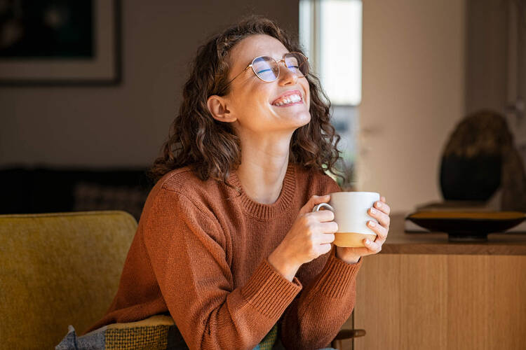 Eine Frau sitzt gemütlich auf dem Sofa und trinkt ihren Kaffee.