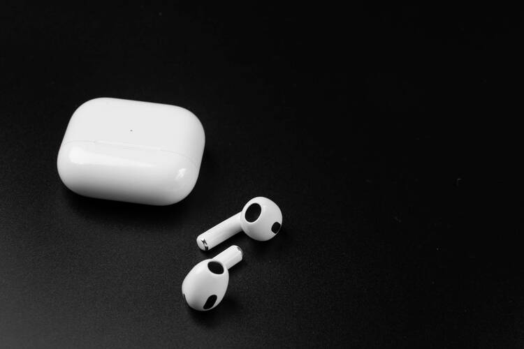 AirPods und Ladecase liegen auf einer schwarzen Fläche.