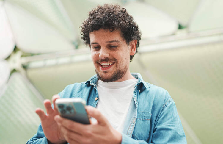 Eine Person hält ein Handy in der Hand und lächelt dabei. 