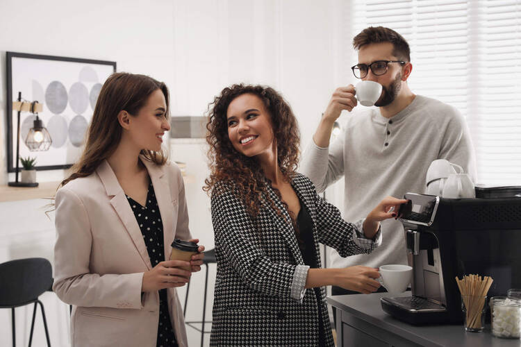 Drei Personen trinken Kaffee und stehen um eine Kaffeemaschine herum