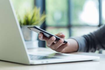 Person sitz mit ihrem iPhone vor einem MacBook 