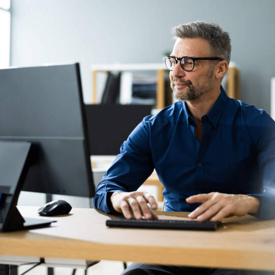 Ein Mann sitzt am Schreibtisch und schaut auf den Bildschirm seines PCs.