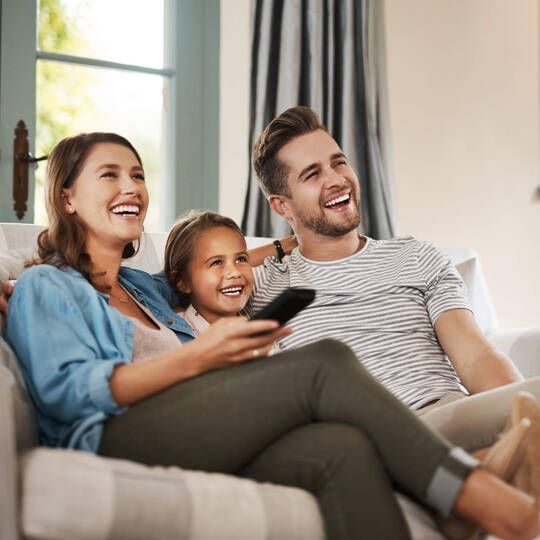 Eine Familie sitzt auf dem Sofa und schaut TV. 