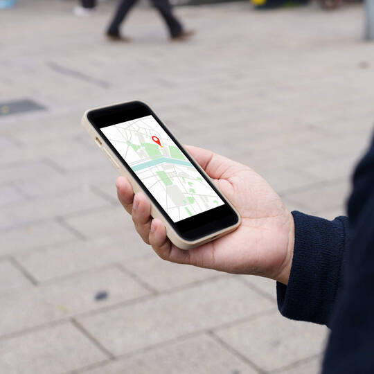 Eine Person hält ein Handy in der Hand und hat eine Karten-App geöffnet.