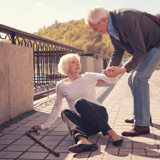 Seniorin liegt am Boden und ein Mann hilft ihr wieder auf